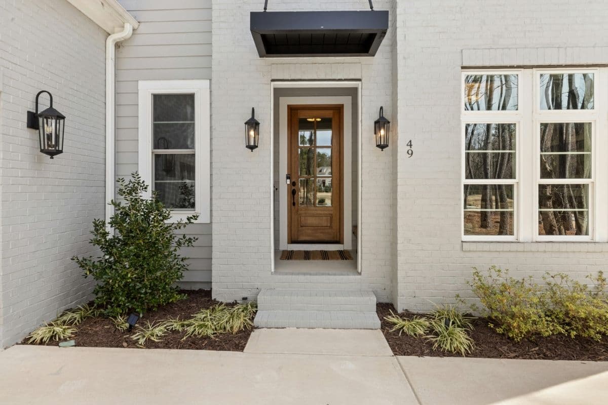 Painted white brick entryway with a stained wood entry door, full-length glass panel and black carriage lanterns