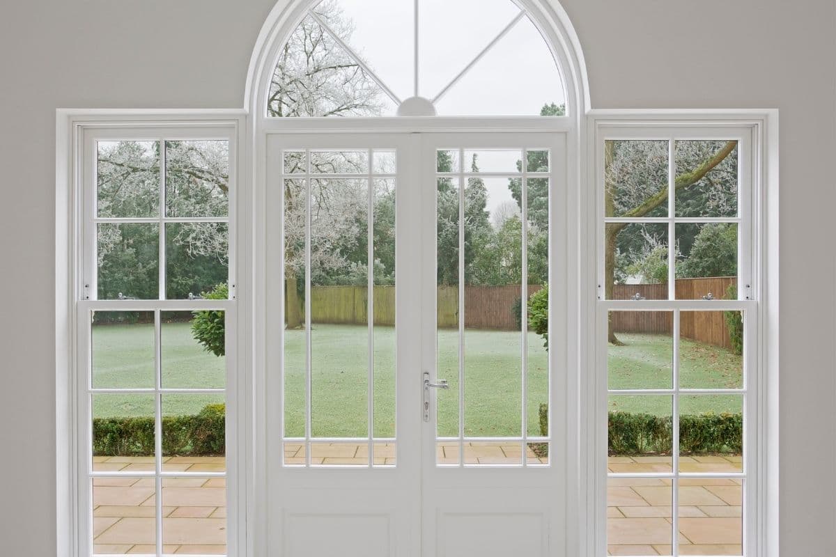 Interior view of white French patio doors with divided-light glass beneath an arched transom window, flanked by double-hung windows