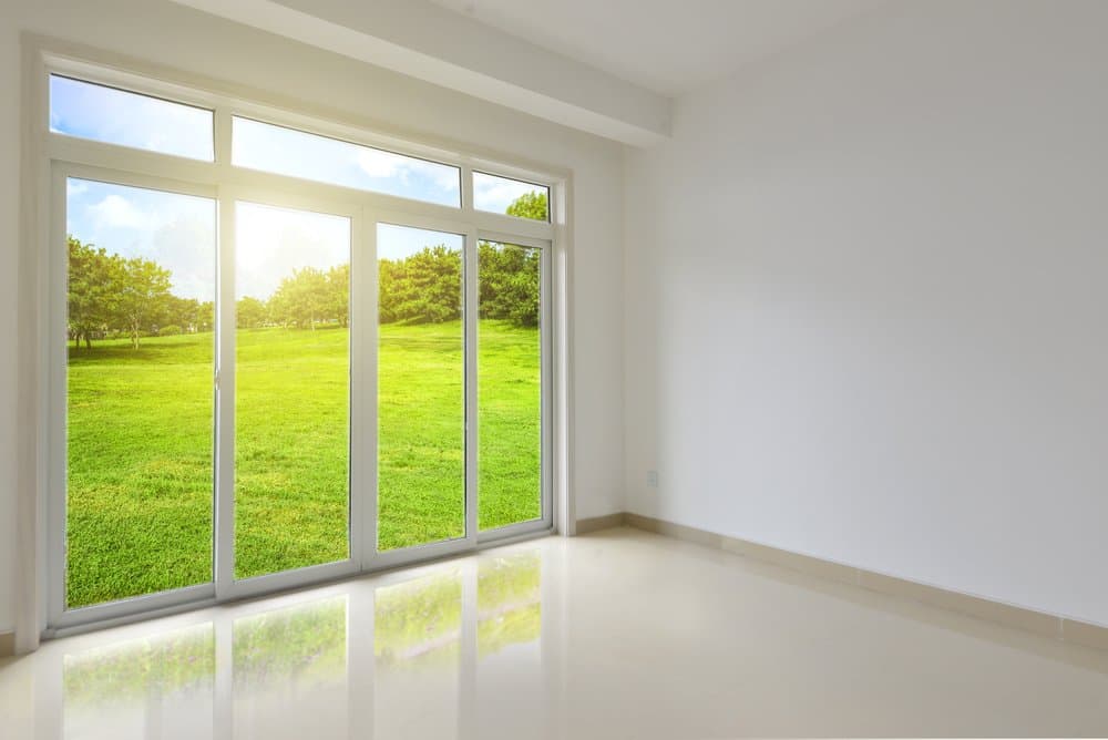 Floor-to-ceiling sliding glass window wall with transom lites opening onto a sunlit lawn